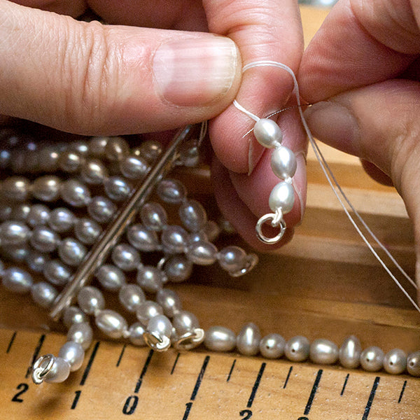 Two hands holding a multi strand pearl necklace with sterling silver spacers.  The hands are string a length of freshwater grey pearls.